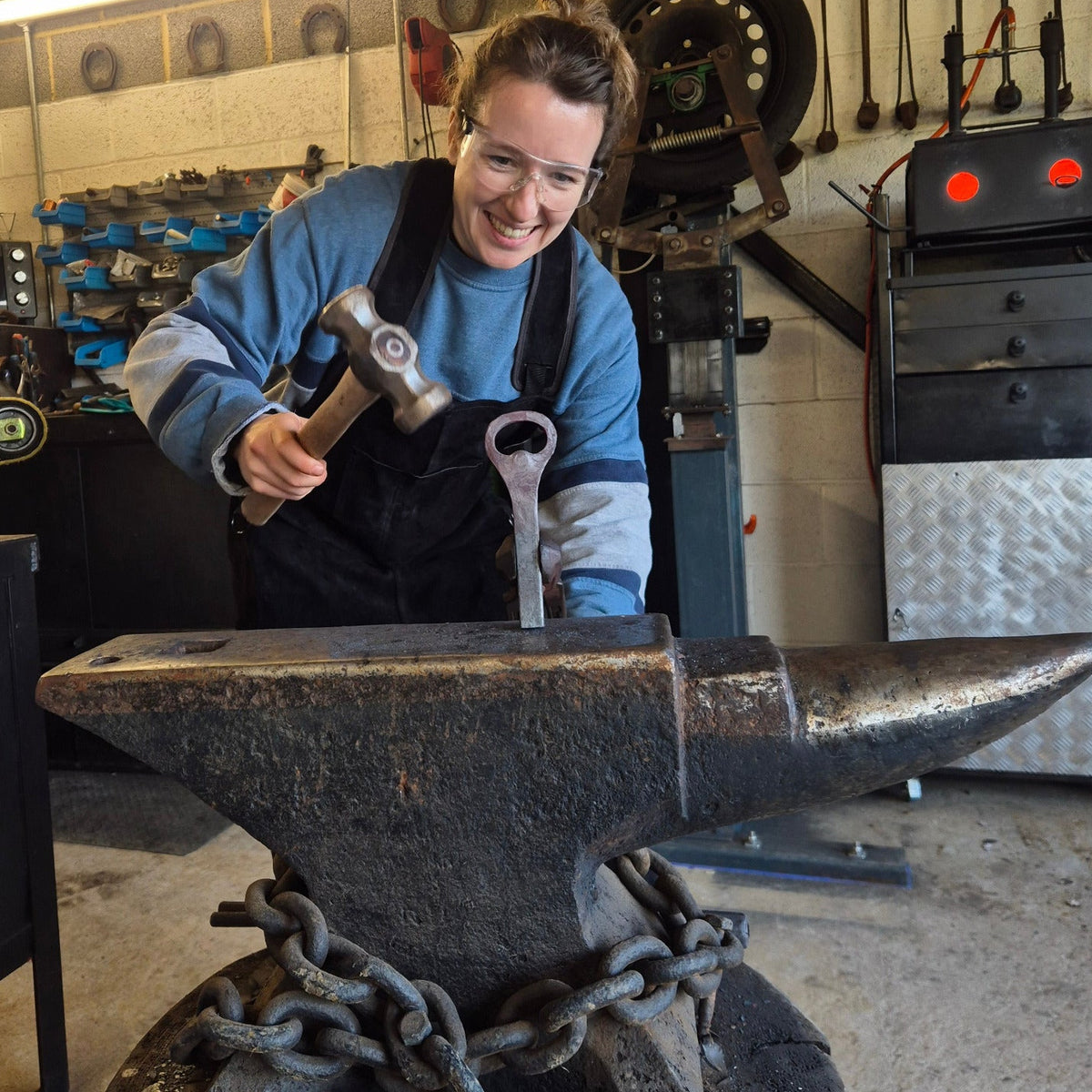 Person working with hammer and metal in the forge, making a bottle opener